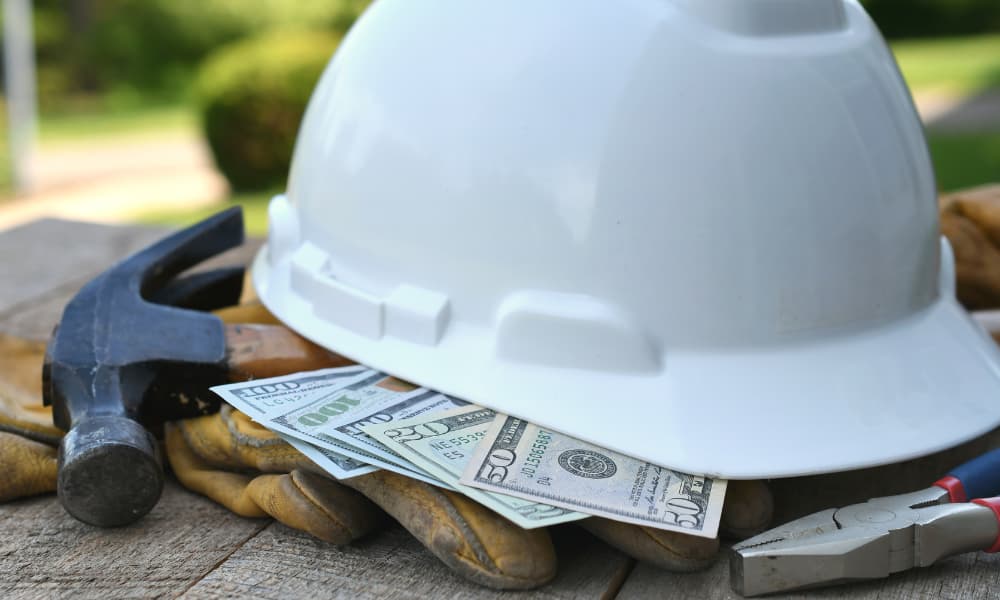 A hard hat on a table with construction tools and money.