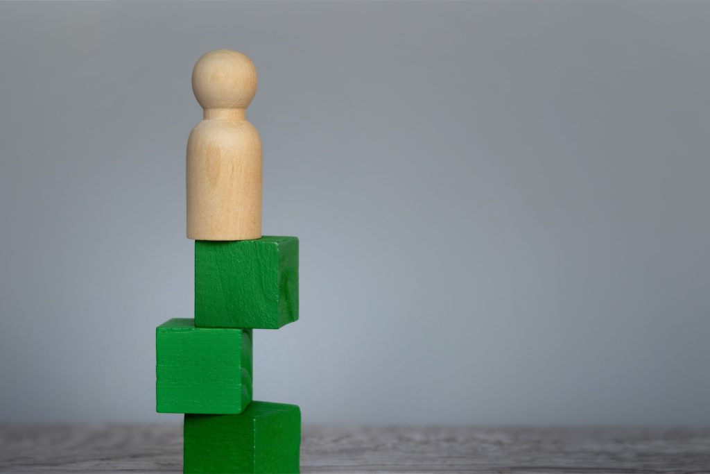 An abstract wooden figure block on top of three green building blocks.