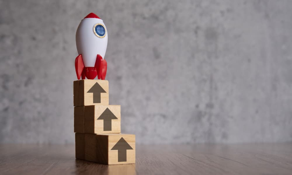 A stack of wooden blocks printed with up arrows leading to a model rocket ship.