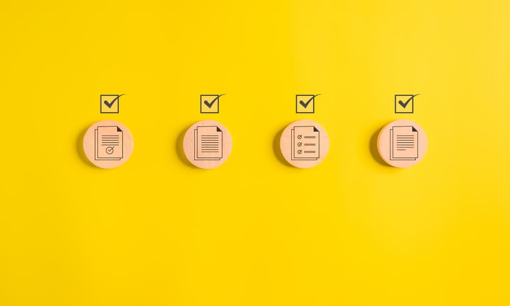 Four checked off document icons on light wooden circles on a yellow background.