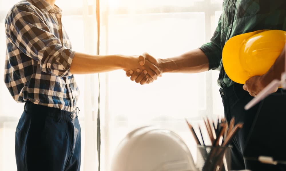 A construction worker shakes hands with a new client in a brightly lit office